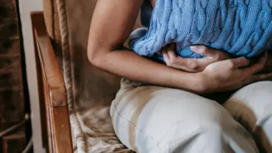 Mulher sentada no sofá com as mãos sobre a barriga, com dor na boca do estômago