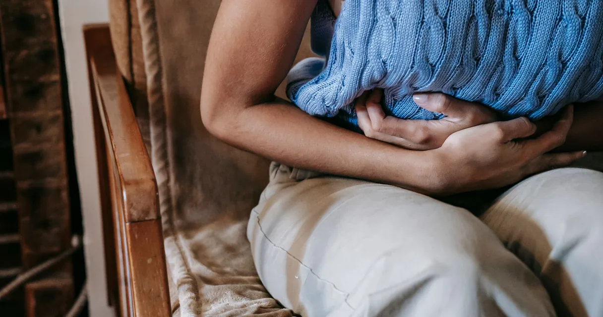 Mulher sentada no sofá com as mãos sobre a barriga, com dor na boca do estômago